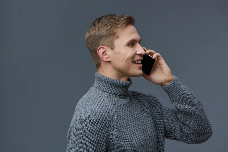 smiling man talking smartphone wear grey knit sweater side view isolated on grey background communication digital nomad lifestyle technology concept