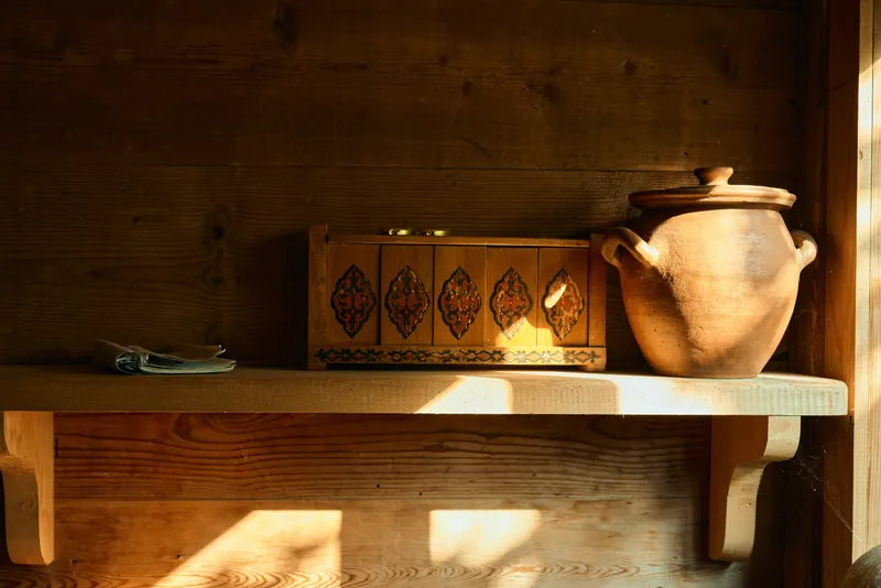Shelf with a wooden box and clay jar bathed in warm light, a rustic interior scene highlighting simple storage, vintage decor and homely atmosphere.