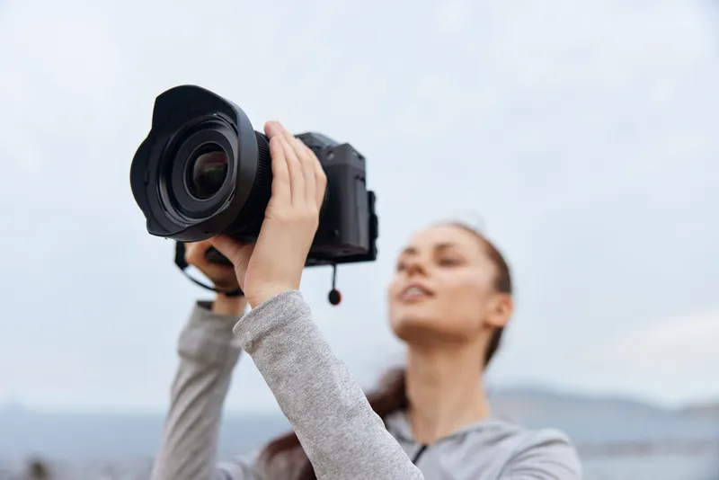 Young woman confidently taking photos outdoors with a professional camera, wearing casual sportswear, exuding creativity and enthusiasm, perfect for photography enthusiasts