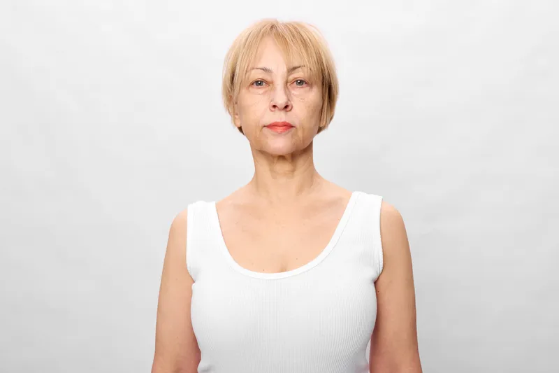 Elderly woman portrait in studio, aging, wellness, skincare, health, confidence, lighting, soft light, short blonde hair, white top, calm neutral expression
