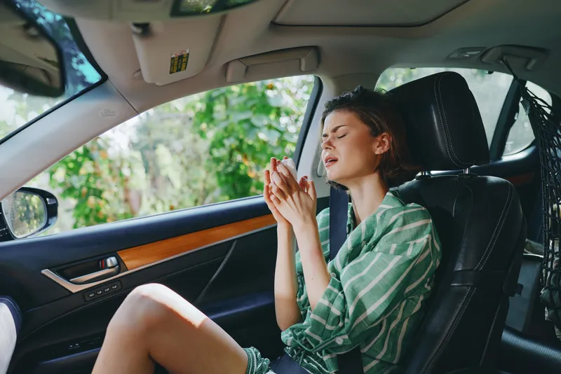 Young woman sits in a car seat with eyes closed, hands clasped in prayer, capturing a peaceful, reflective moment inside a parked vehicle.