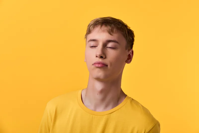 Calm, relaxation, serenity, yellow, closed eyes, peaceful, studio, emotion, simplicity, monochrome mood with a relaxed youth on a warm yellow backdrop, conveying stillness, inner balance, and gentle