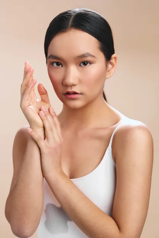 asian woman poses in a studio portrait with a calm gaze and poised hands, conveying elegance, softness, and quiet confidence in a clean, minimalist setup.