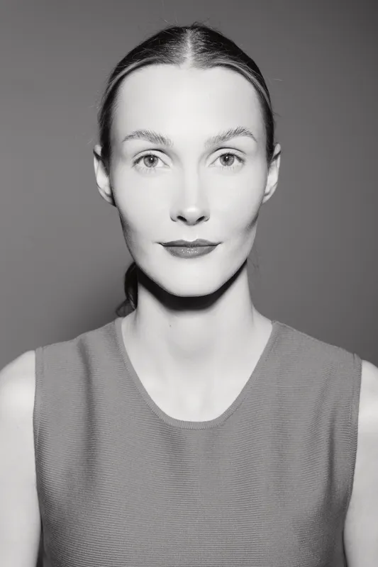 Portrait of a young Caucasian woman with fair skin and brown hair tied back, wearing a sleeveless top. Studio lighting highlights her calm and confident expression.