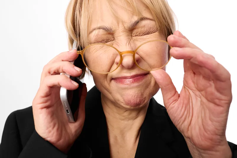 Elderly woman adjusting glasses, smiling while holding a phone near ear, communication, vision healthcare care, vision support, white studio background, soft light portrait