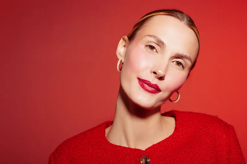 Portrait of a confident woman with red lipstick and hoop earrings wearing a red sweater against a red background. Concept of beauty, fashion, and elegance in studio lighting.