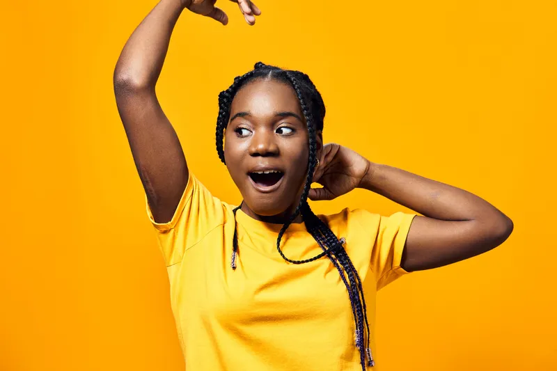 Joyful Black girl expressing excitement in a vibrant yellow t shirt against a bright yellow background, showcasing energetic emotions and playful vibes