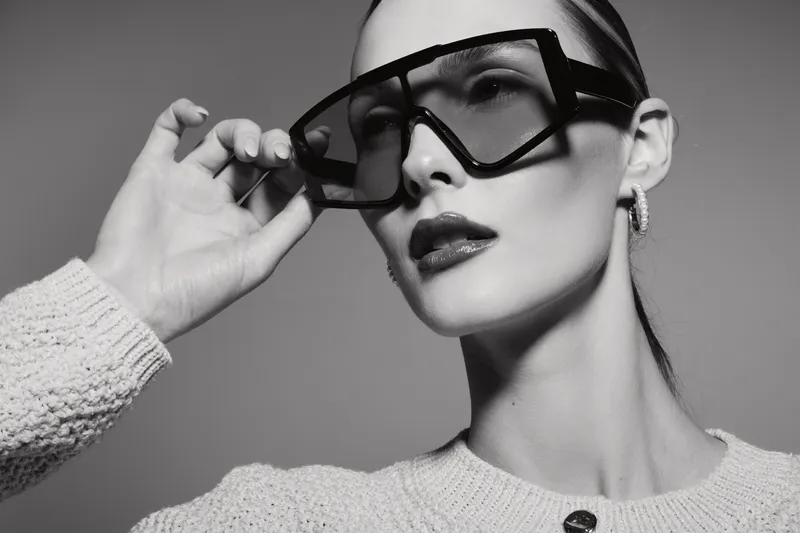 Portrait of a white woman with pale skin wearing oversized black sunglasses and a knitted sweater. Stylish minimalistic fashion concept in monochrome.