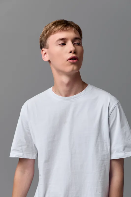 Man wearing a white t shirt against a neutral gray backdrop, casual studio styling, clean minimal look suitable for fashion, lifestyle and stock photography projects