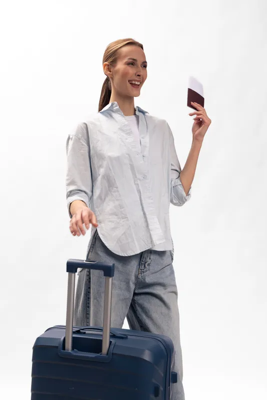 Happy young woman in casual clothes holds passport and ticket, walking with suitcase. Travel concept for vacation, tourism, and trip planning with positive mood.