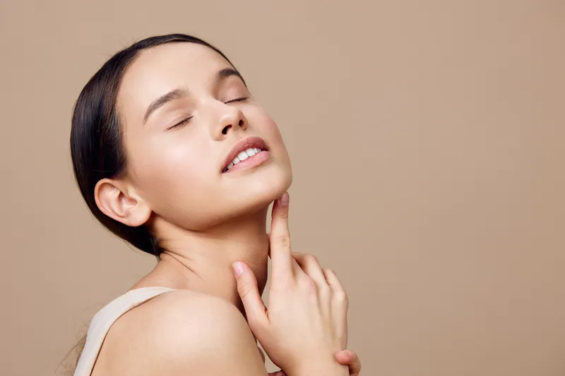 Serene woman with natural makeup posing against a beige background, showcasing healthy skin and a relaxed expression