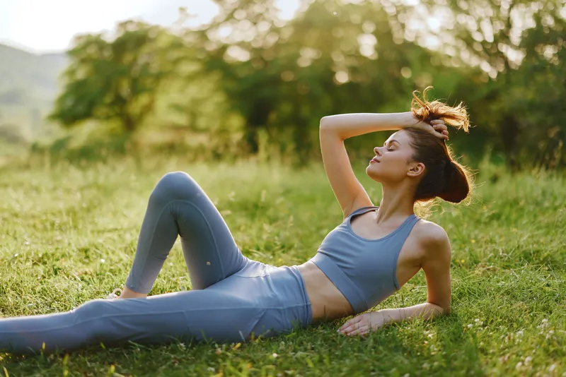 Young athletic woman in a blue sports outfit enjoying a sunny day in a beautiful green landscape, promoting healthy lifestyle and wellness concepts