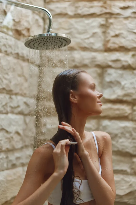 young woman showering outdoors under rainfall with wet hair, serene expression, natural stone background, wellness and self-care moment captured
