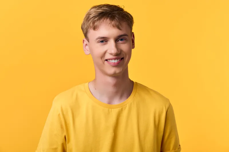 Smiling man in a yellow t shirt stands against a bright yellow background, presenting a casual, friendly vibe suitable for lifestyle, fashion, and wellness themes in studio photography