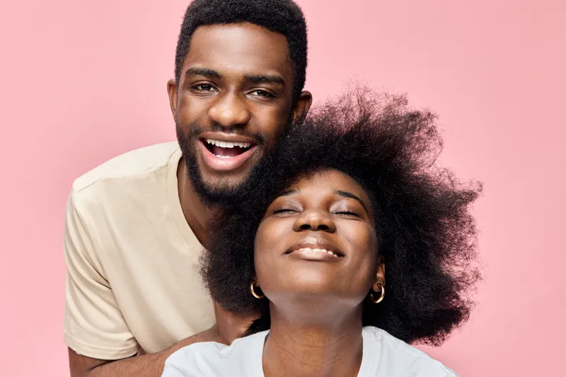Happy young couple with joyful expressions against a pink background, showcasing love and connection, perfect for themes of happiness and relationships