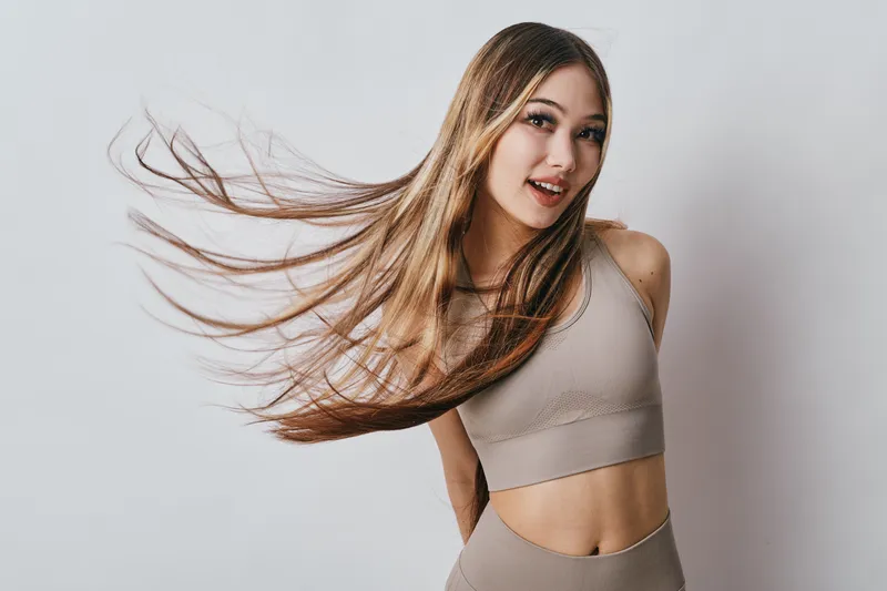 Young woman with long flowing hair and athletic wear posing with smile on light background. Healthy lifestyle, fitness model and casual style with natural beauty and movement.