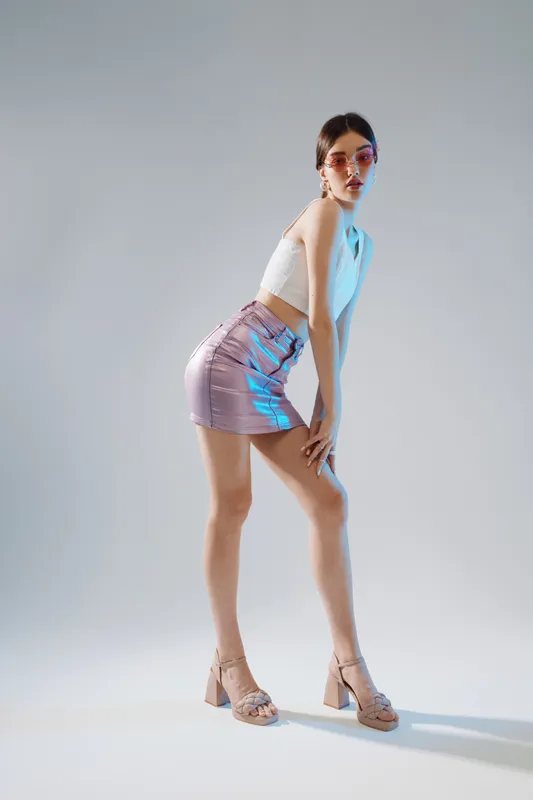 Young woman beauty fashion model poses in a shiny skirt and white top on a light background. Concept of style, elegance, and modern trends in fashion photography.