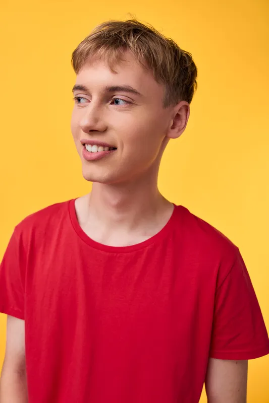 Young man in a red shirt stands against a bright yellow background, casual studio vibe, clean lighting, fashion style, approachable and friendly expression.