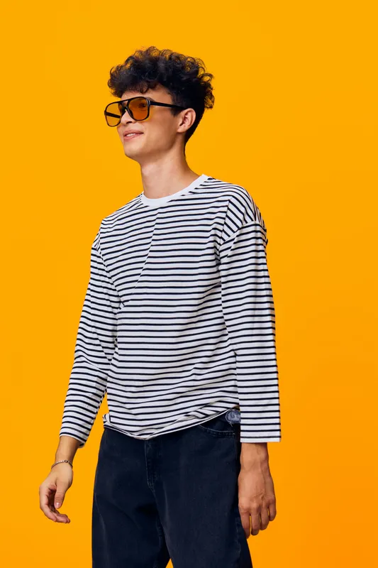 Young man wearing sunglasses and a striped shirt standing confidently against an orange background with a casual and modern style.