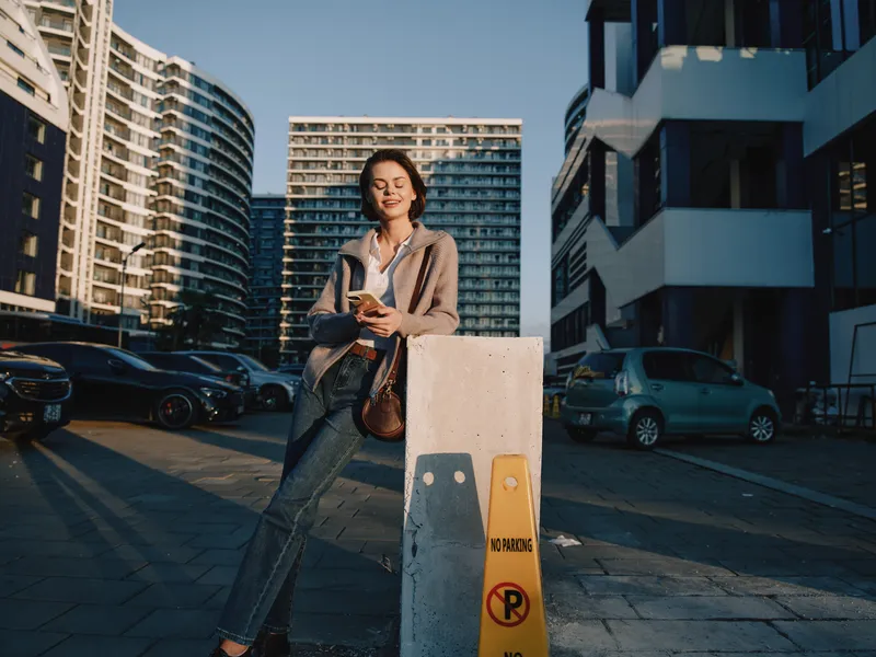 A cheerful professional woman is seen texting in a modern urban setting. She smiles, appears engaged, and creates a positive, dynamic atmosphere suitable for business, networking, and contemporary