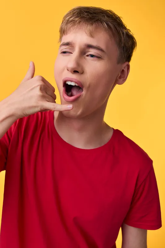 Young man in a red shirt with a playful ear gesture and open mouth, bright yellow backdrop, casual lifestyle vibe, focused on communication and energy for social media and advertising use