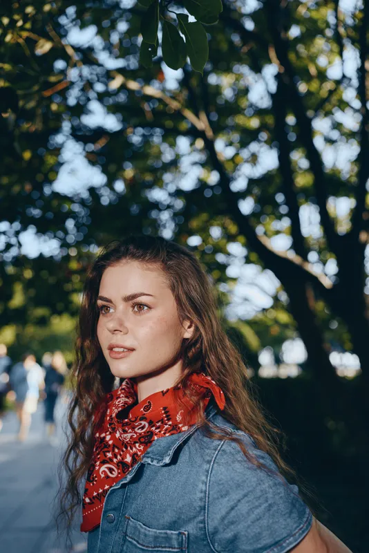 lifestyle woman in modern boho-western denim street style with red bandana, natural light, relaxed expression, film color tones creating warm, casual atmosphere