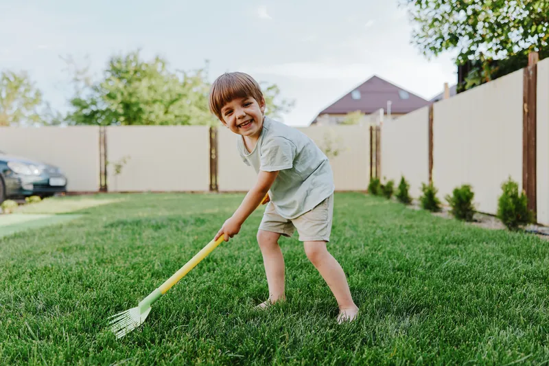 Happy boy playing in the garden with a rake, enjoying outdoor activities, sunshine, and nature. Perfect for family and childhood themes.