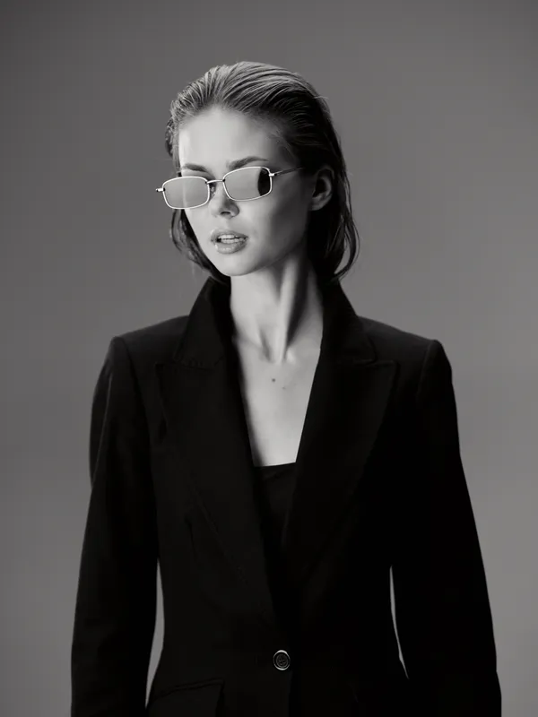 Black and white portrait of a stylish woman wearing sunglasses and a black blazer with a confident expression.