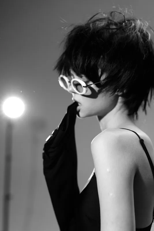 Black and white portrait of a stylish woman with short hair wearing sunglasses and gloves in a dramatic lighting setting