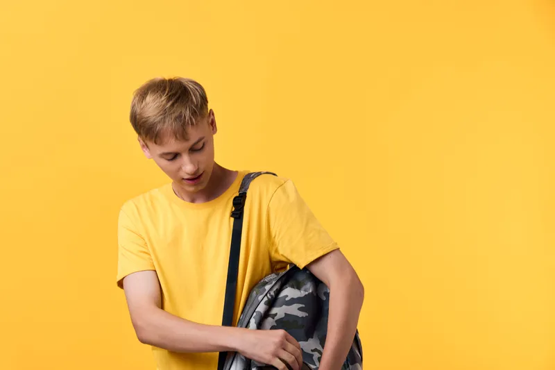 Student wearing a yellow t shirt with a camouflage backpack against a vibrant yellow background, casual style for everyday travel, urban exploration, and modern youth attire