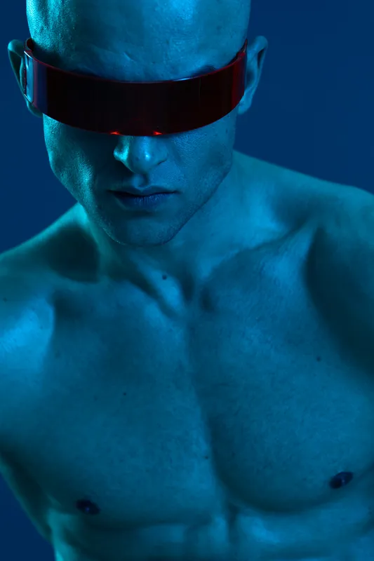 Striking image of a man wearing futuristic red-tinted glasses, showcasing unique features in a bold blue light—perfect for modern and tech-themed projects.