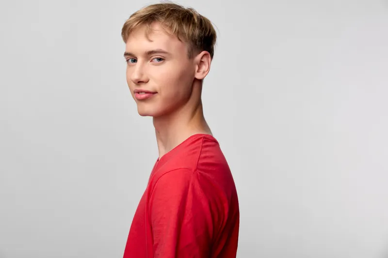 Young man wearing a red shirt in a clean studio with soft lighting, side profile view against a neutral backdrop, conveying confidence and focus for lifestyle and fashion stock imagery