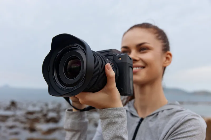 Young woman with a camera enjoying photography outdoors, capturing nature s beauty, wearing casual sports attire against a scenic backdrop