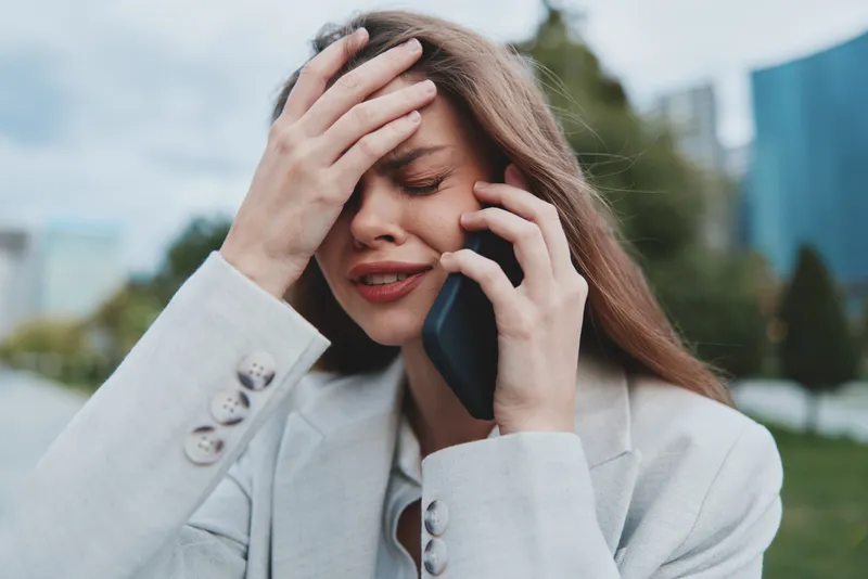 Stressed woman in business suit talking on smartphone outdoors showing anxiety and financial crisis emotions