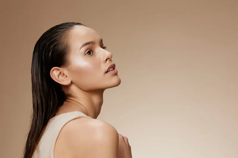 Elegant portrait of a beautiful woman with natural makeup and wet hair, showcasing healthy skin tones against a soft beige background