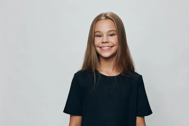 Girl portrait with long hair smiling wearing black shirt standing against gray background looking happy confident and relaxed for casual lifestyle and youth concept