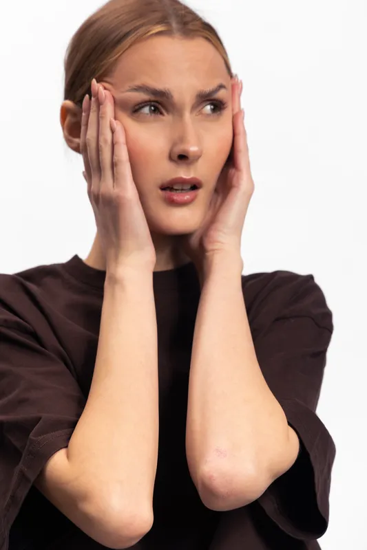 Young woman in black shirt looks worried and stressed holding her face with both hands. Isolated on white background, concept of anxiety, concern, and emotional distress.