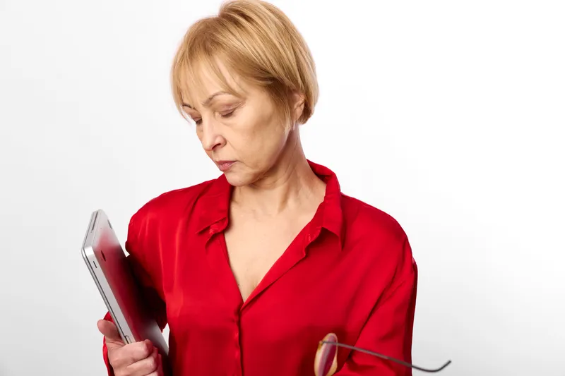 Woman senior in red shirt holding smartphone, reading with glasses, concentration and worry on face, isolated indoor portrait on white background