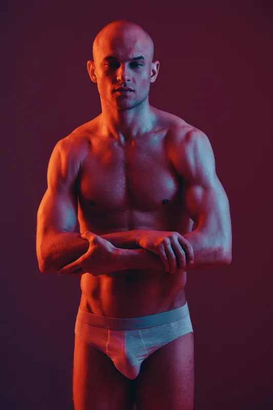 Muscular man posing confidently in a dramatic light setup, showcasing his physique. The image emphasizes strength and artistic expression in a vibrant color palette.