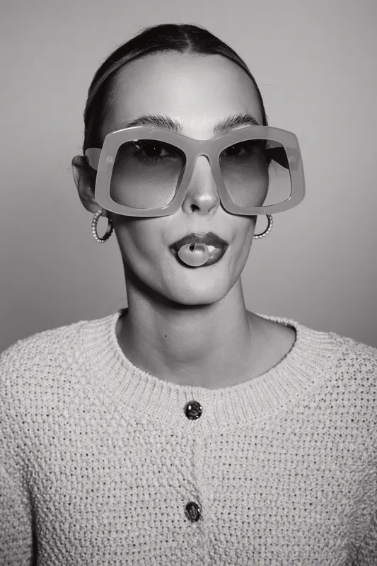 Stylish young white woman with pale skin wearing large sunglasses and hoop earrings posing with tongue out.