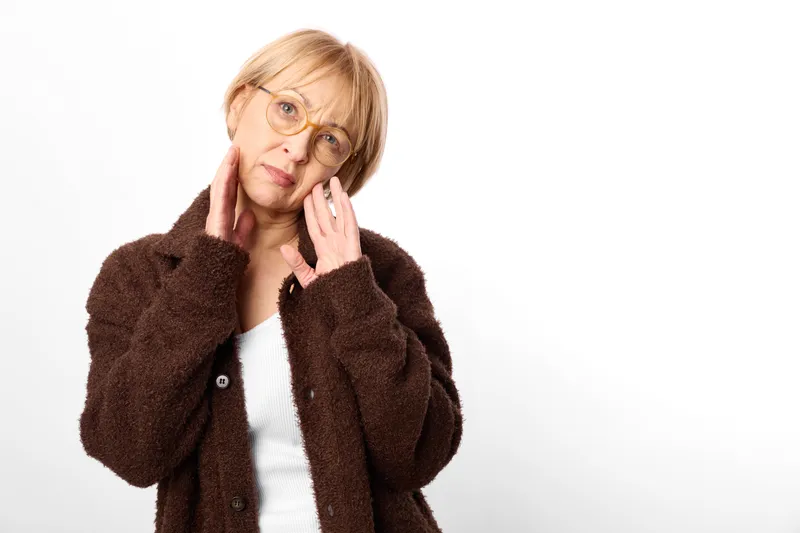 Adult woman portrait with worried expression touching her cheek and face with hands, wearing glasses, isolated on white background, concept of stress and anxiety, mental health