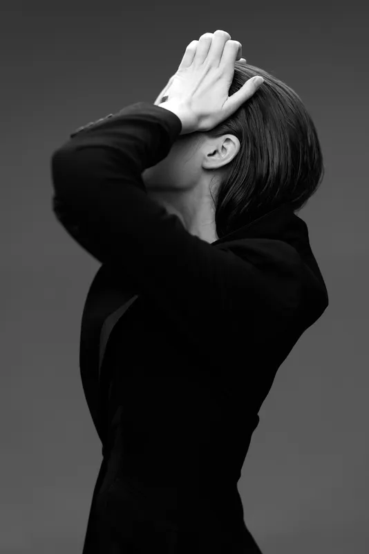 Black and white portrait of a woman covering her face with her hand in a dramatic pose.