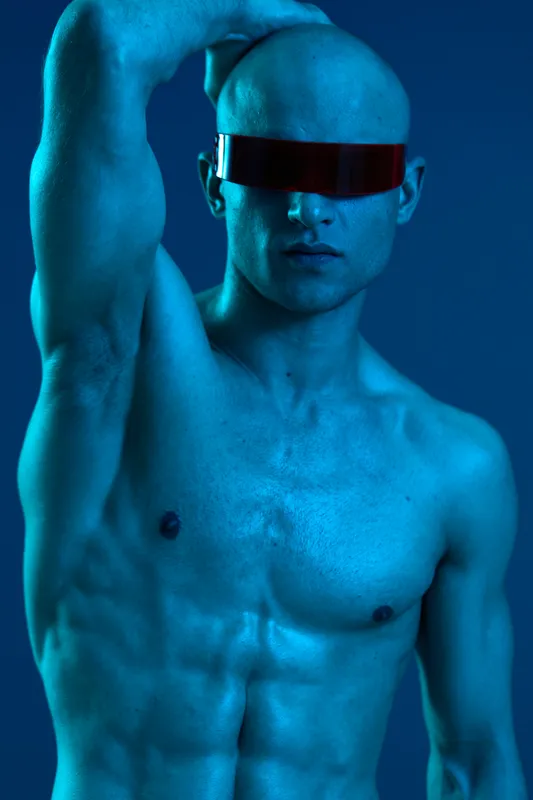 Muscular man posing in futuristic sunglasses, showcasing a striking blue light effect. The image has a captivating, bold atmosphere that draws attention.