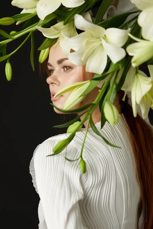 Elegant model adorned with white lilies, showcasing a serene expression against a dark background, capturing the essence of beauty and nature in fashion photography