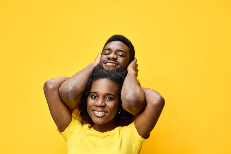 Joyful couple posing together against a vibrant yellow background, showcasing happiness and love through their warm smiles and playful interaction