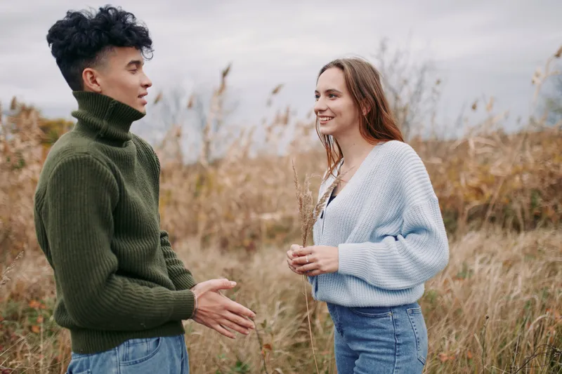 An authentic candid moment between two people sharing a conversation in a natural field, capturing genuine interaction, warmth, and realism in soft daylight.