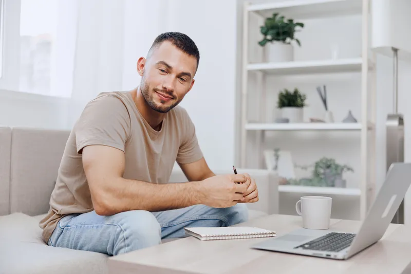 Focused man working on his laptop at home, surrounded by cozy decor and greenery, creating a relaxed atmosphere for productivity. Perfect for modern lifestyle themes.