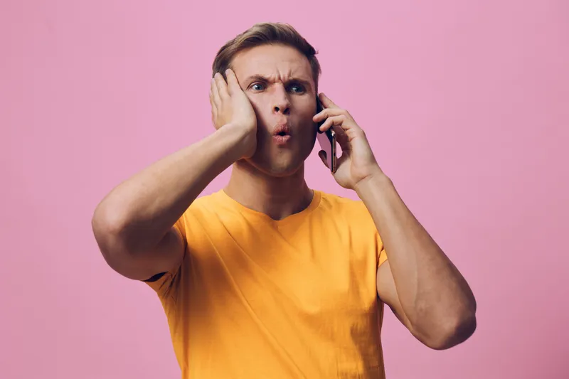 concerned man talking phone surprised shocked emotions casual orange t-shirt pink background digital communication concept