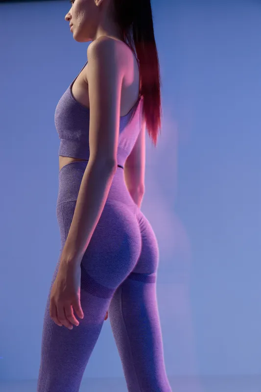 woman sport fitness wearing purple seamless activewear set, standing in profile pose under soft studio lighting with blurred background, healthy lifestyle concept