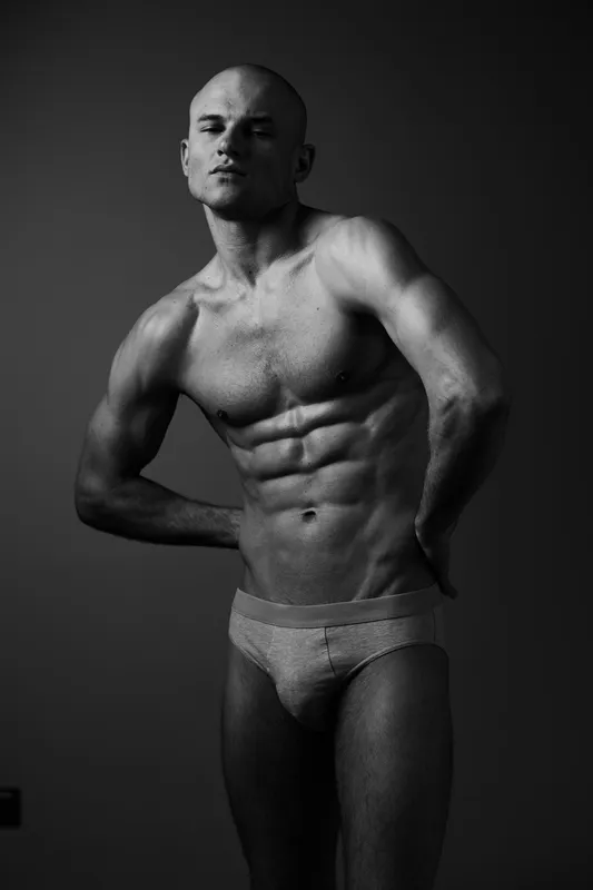 Black and white image of a muscular man posing confidently, showcasing strong physique and expression. The composition emphasizes fitness and strength.